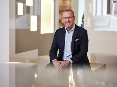 Photo of Lubert Winnecken, seated in office setting smiling, wearing a blue suit jacket, white shirt and glasses.