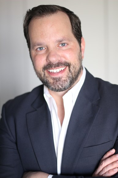 Photo of Greg Rankin, white man with gray and dark short beard with dark hair and wearing dark blazer with white shirt and arms crossed