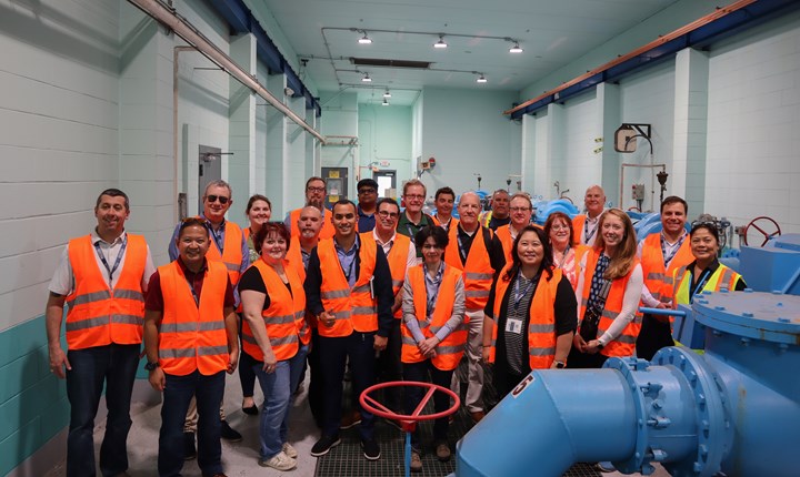 Photo of people in orange safety vests in front of large blue pumps at water treatment plant